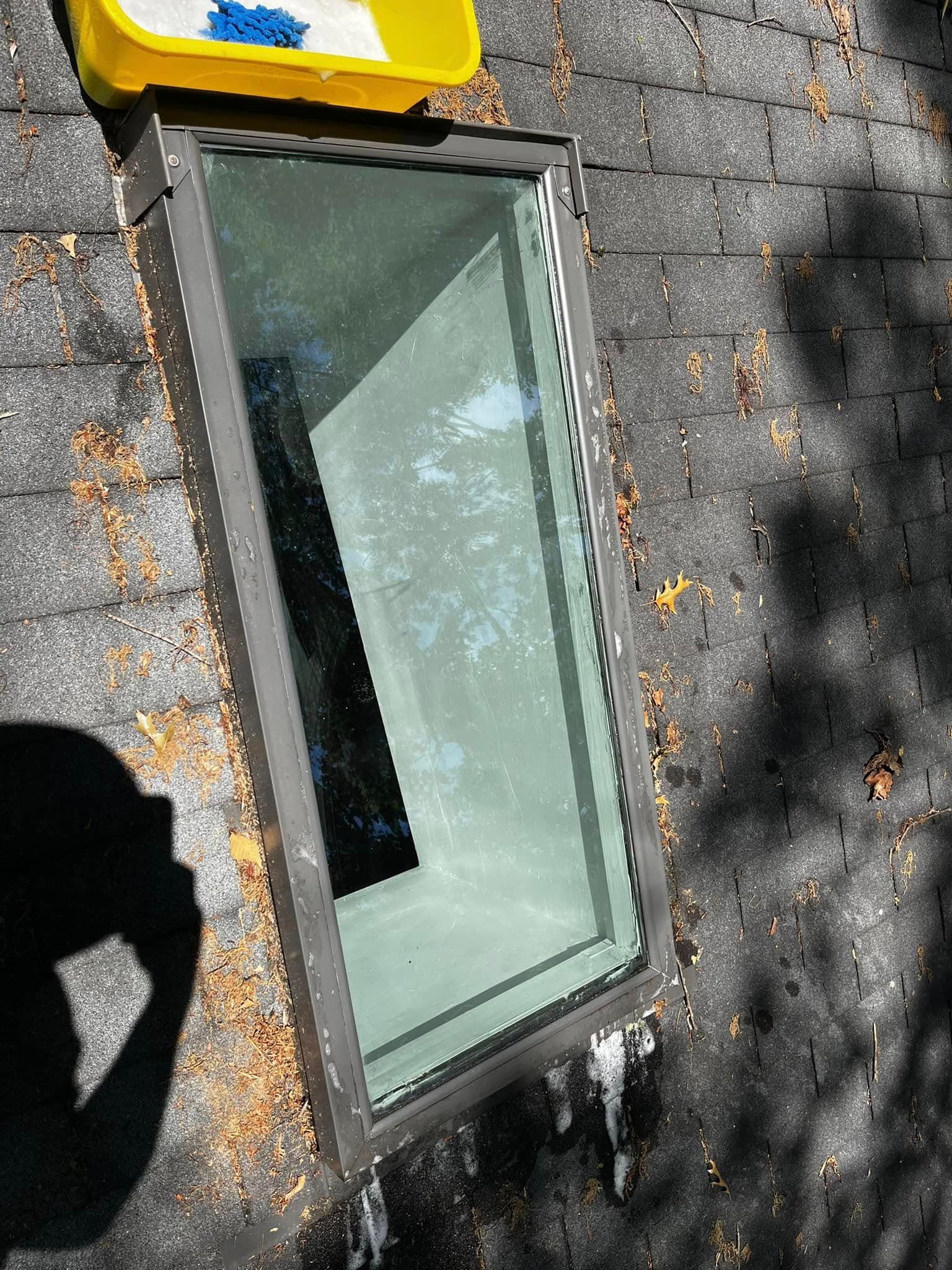 Newly installed window on a sloped roof, surrounded by debris and sunlight shadows.