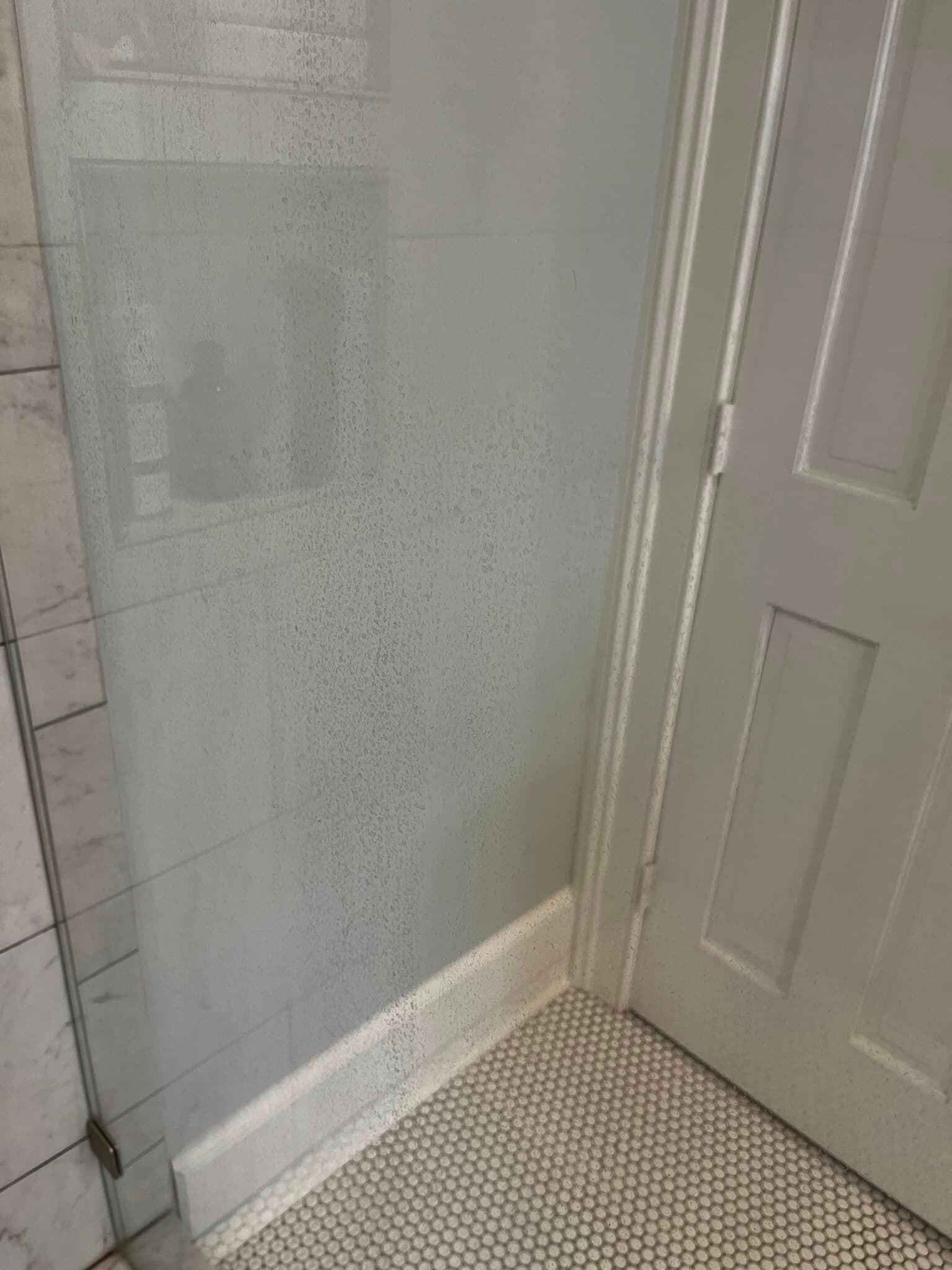Bathroom shower stall with foggy glass and door, tiled floor, and shower supplies visible.