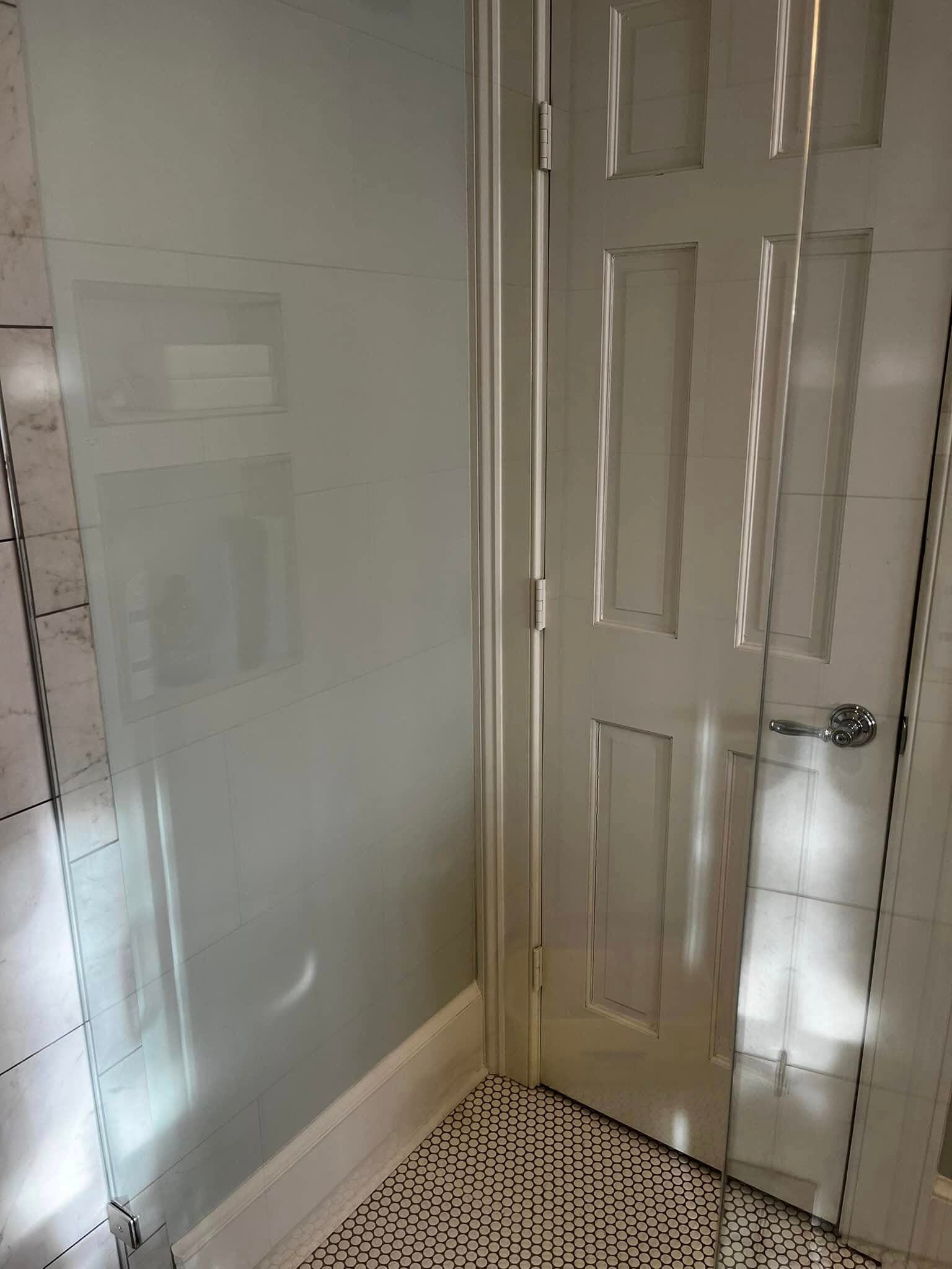 Modern bathroom shower corner with glass enclosure and a closed door, featuring tile accents.